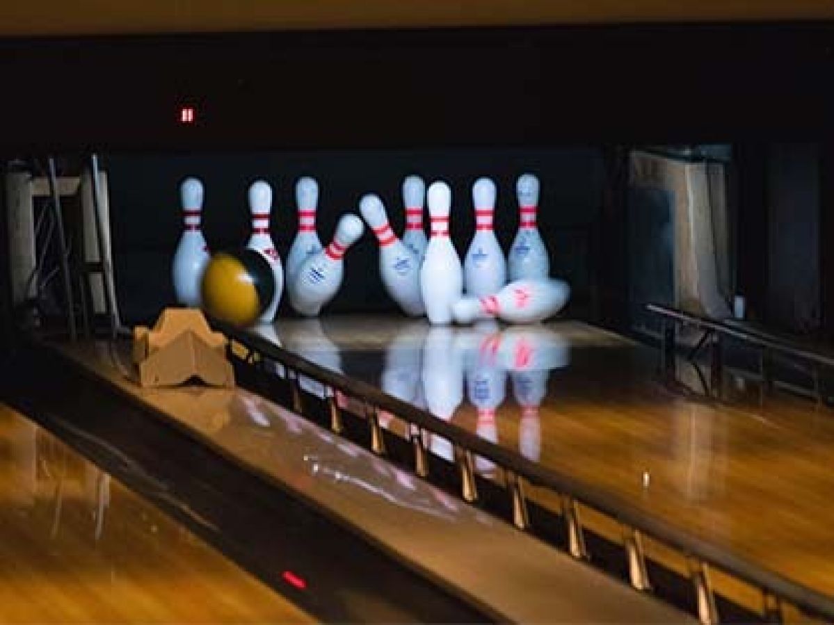 A collection of ten pin bowls being knocked over in a bowling lane by a bowling ball. 