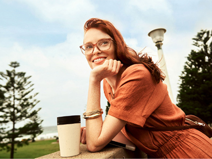 Woman wearing glasses while smiling into the distance and holding her coffee cup.