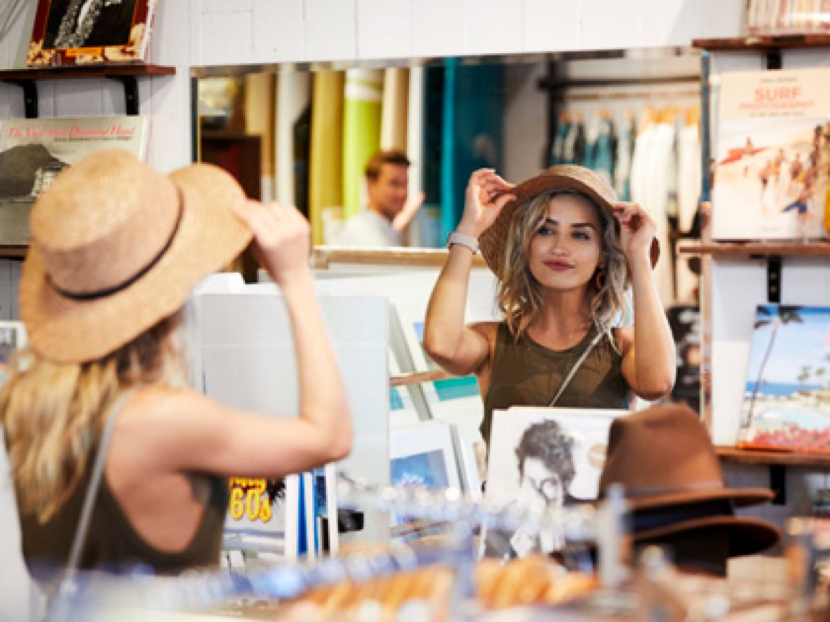 Woman trying on a hat and looking in a mirror.