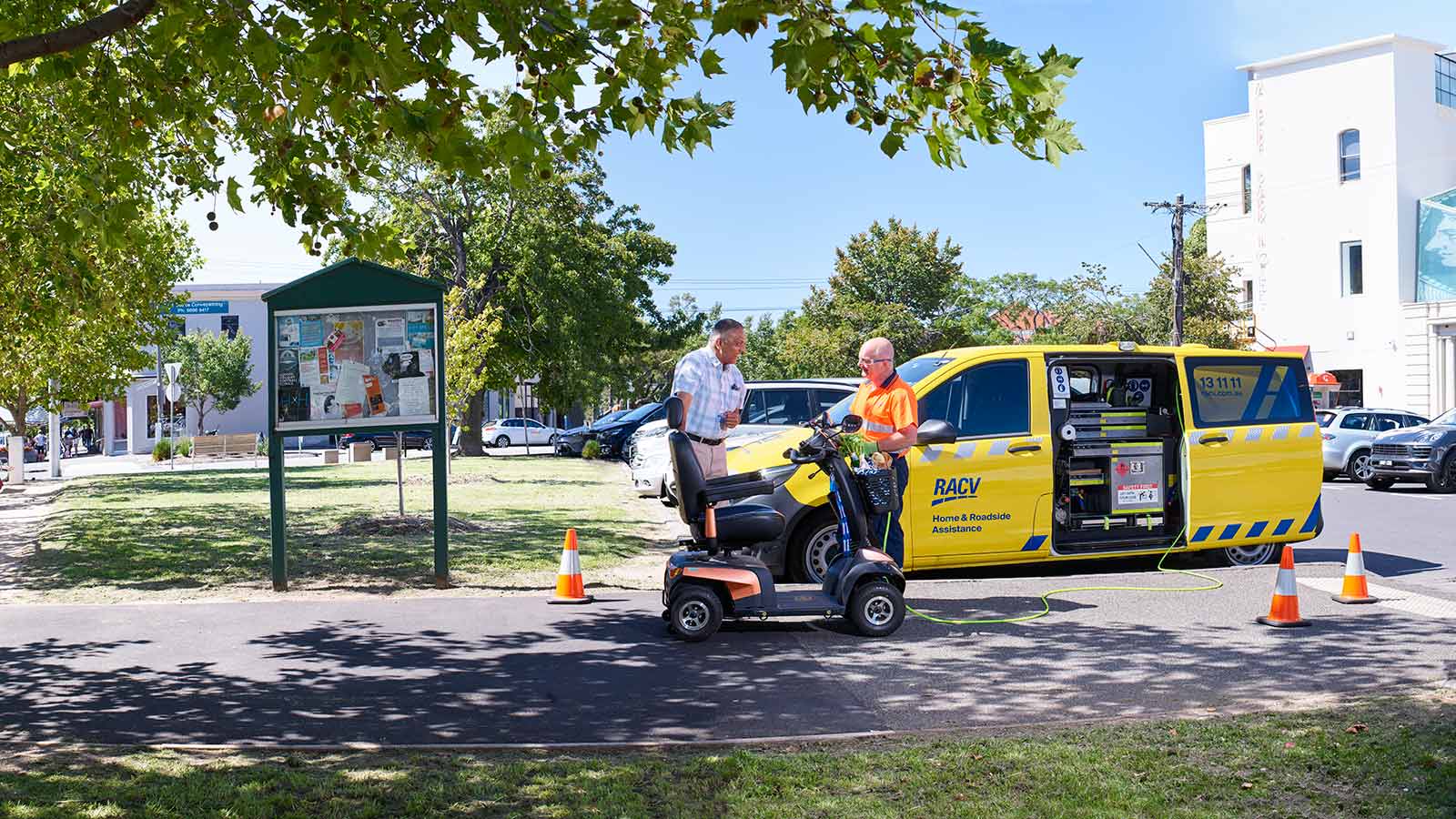 RACV technician fixing a mobility scooter and speaking with a smiling customer, with the RACV yellow patrol van behind them.