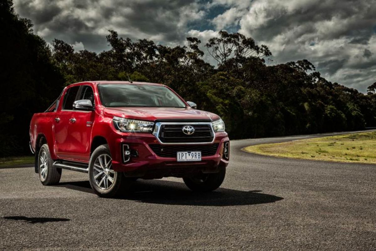 red toyota hilux parked on road in front of trees