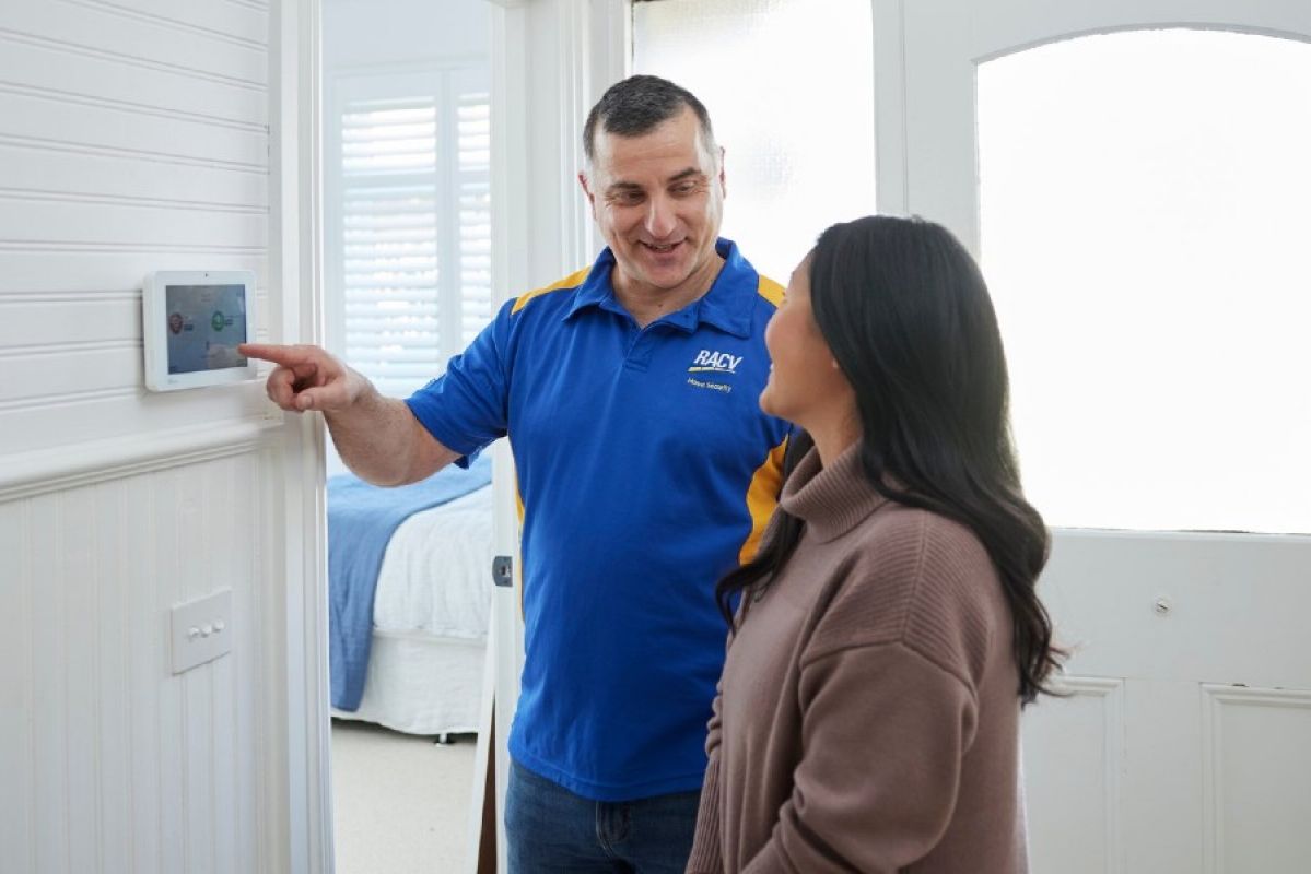 A home security technician showing a woman how her new in-home security system works via the panel inside the house