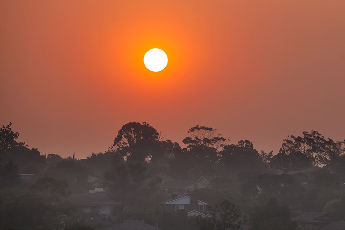 Sun illuminating smoke haze in orange colour over trees and houses in Victoria