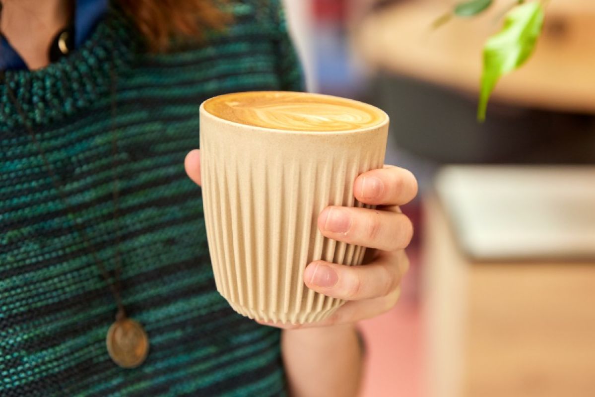 A woman holding a reusable coffee cup fill with a latte