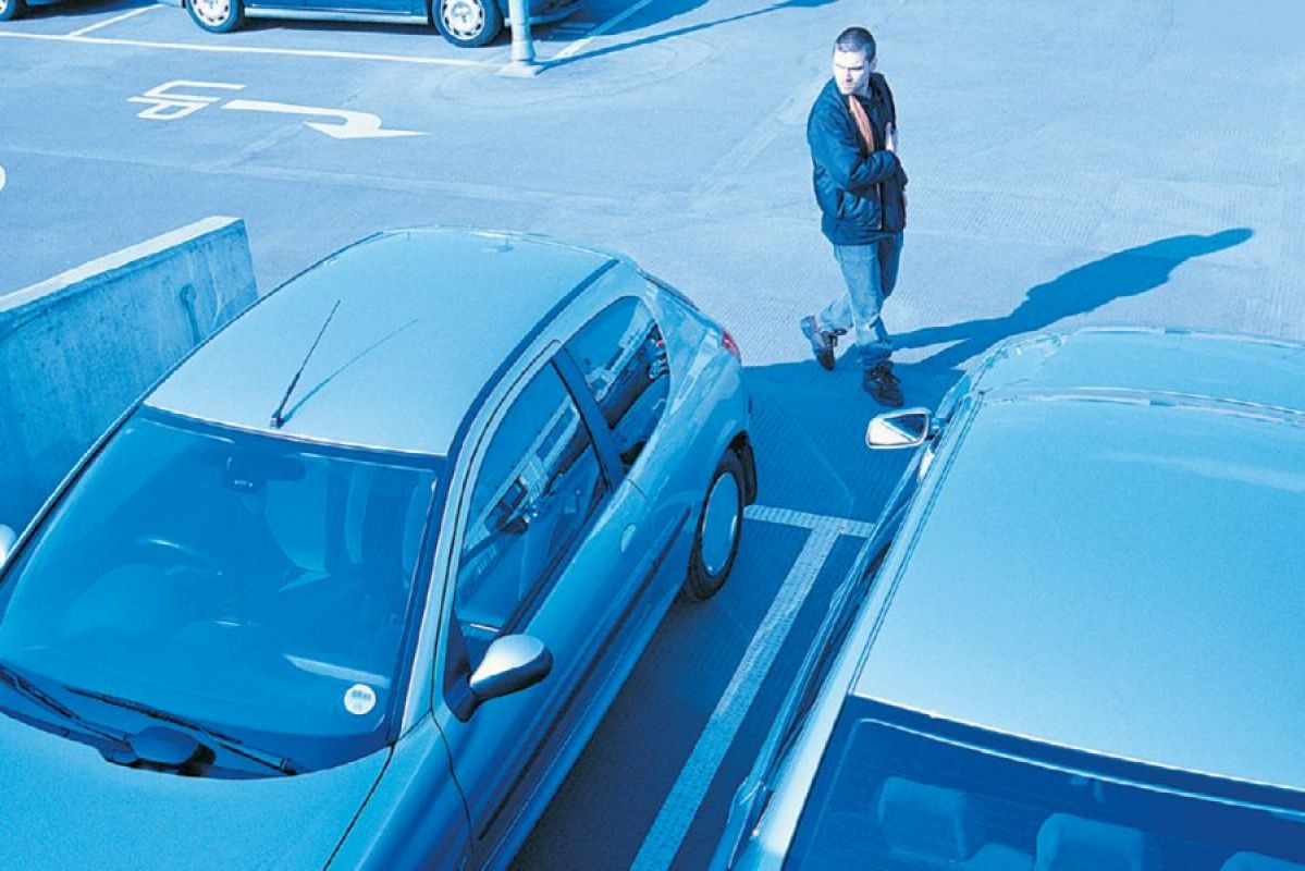 A suspicious man looks at cars as seen on a CCTV camera