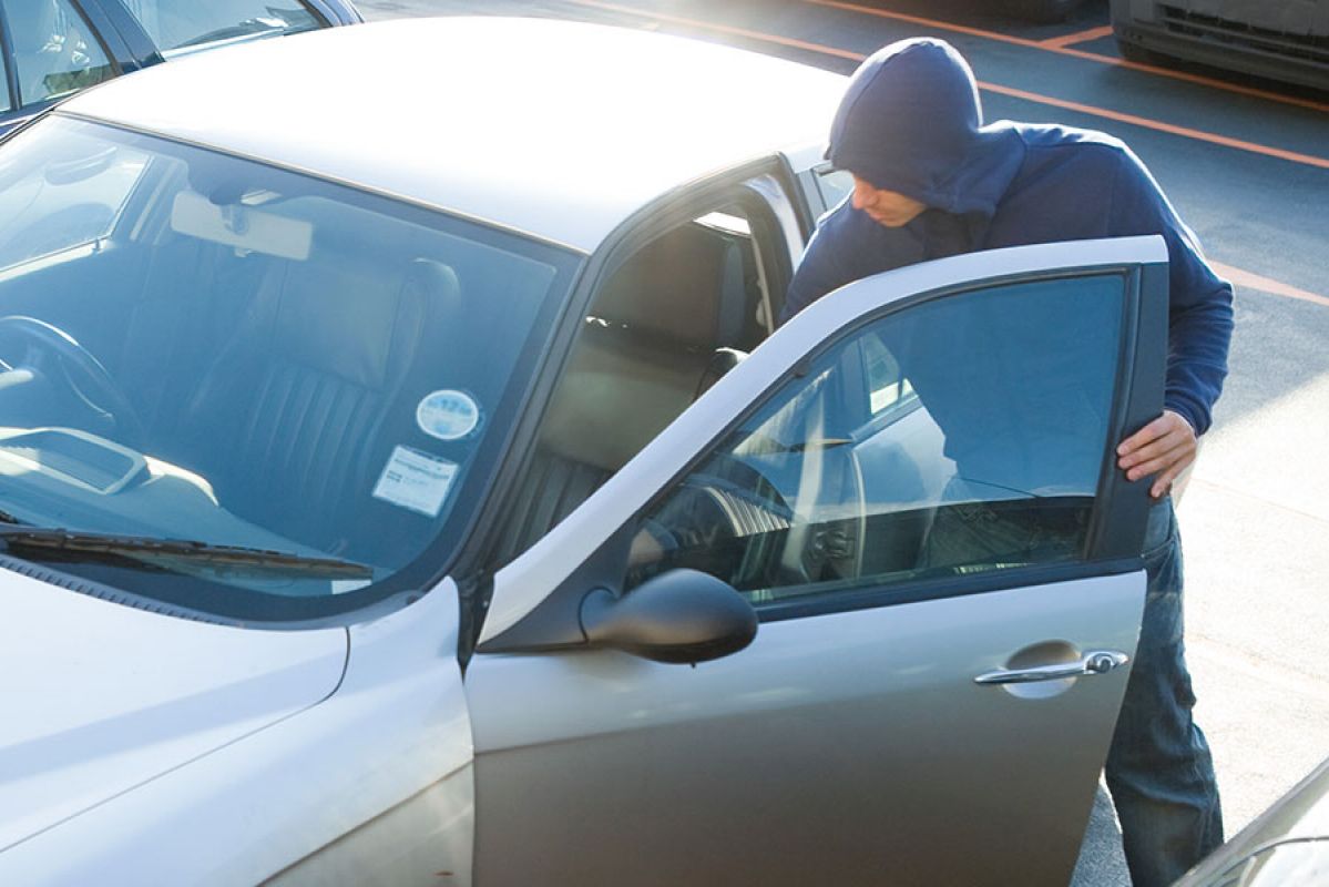 A man wearing a hoodie opening a car door suspiciously