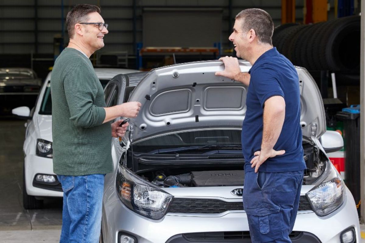 mechanic speaking to car owner in front of car with hood up