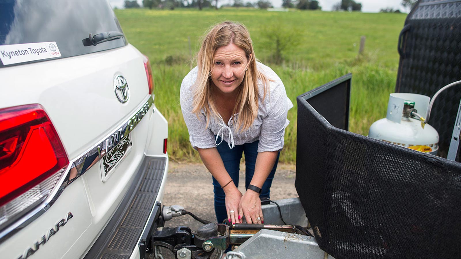 Smiling woman fixing a tow hitch attached to her white Kyneton Toyota.