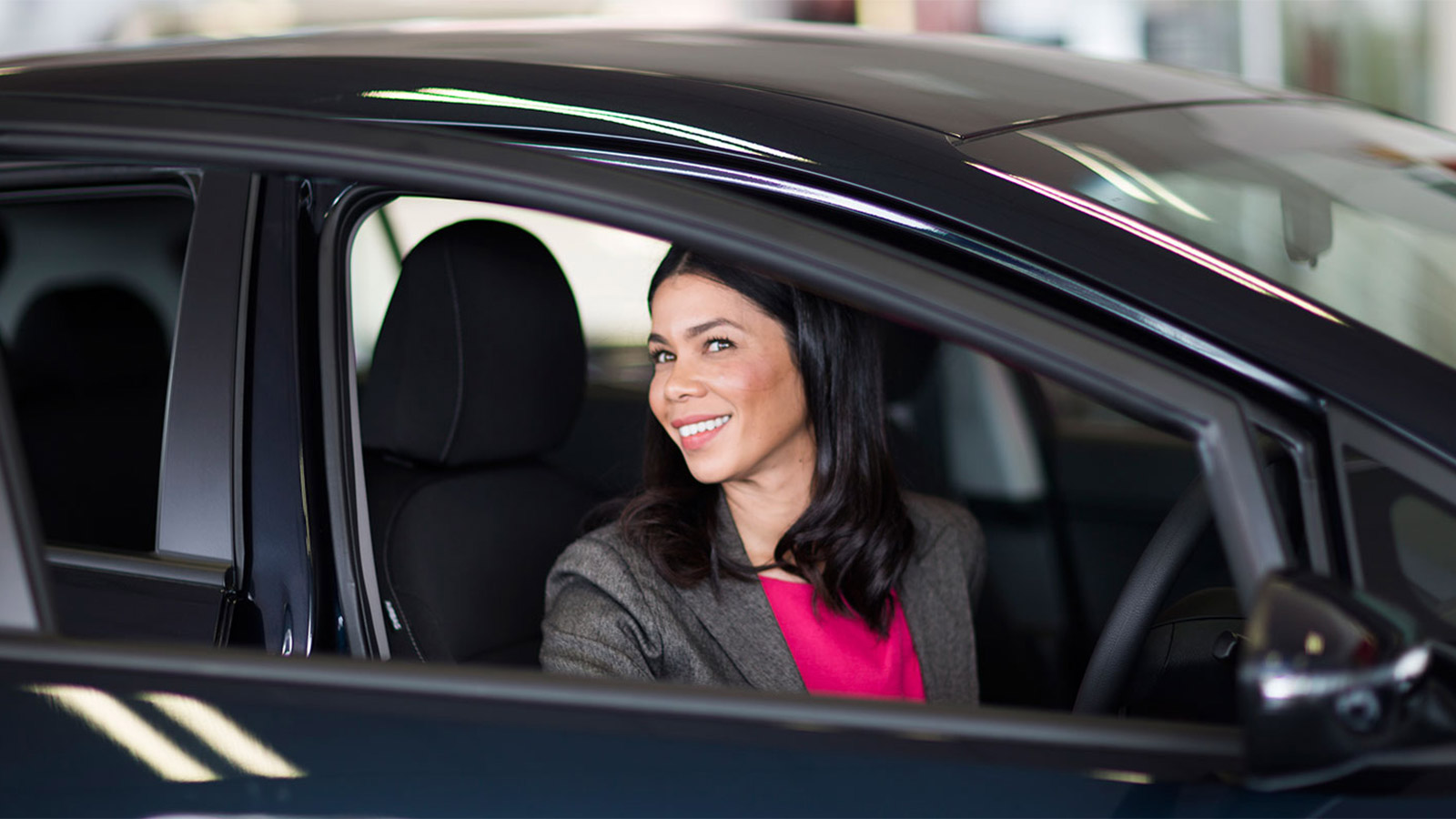 Woman sitting in a black Kia car smiling.