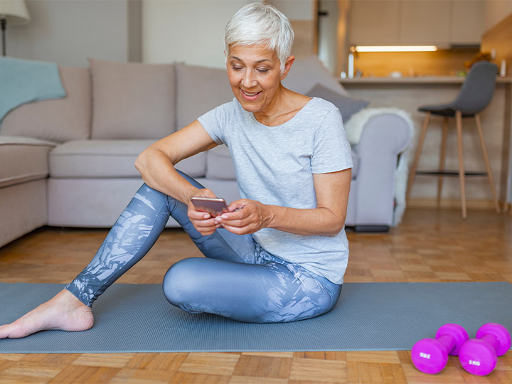 Woman looking at her phone while sitting on a yoga mat.