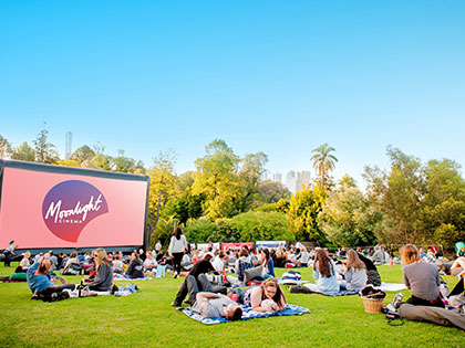 People sitting on a lawn in front of a large film screen
