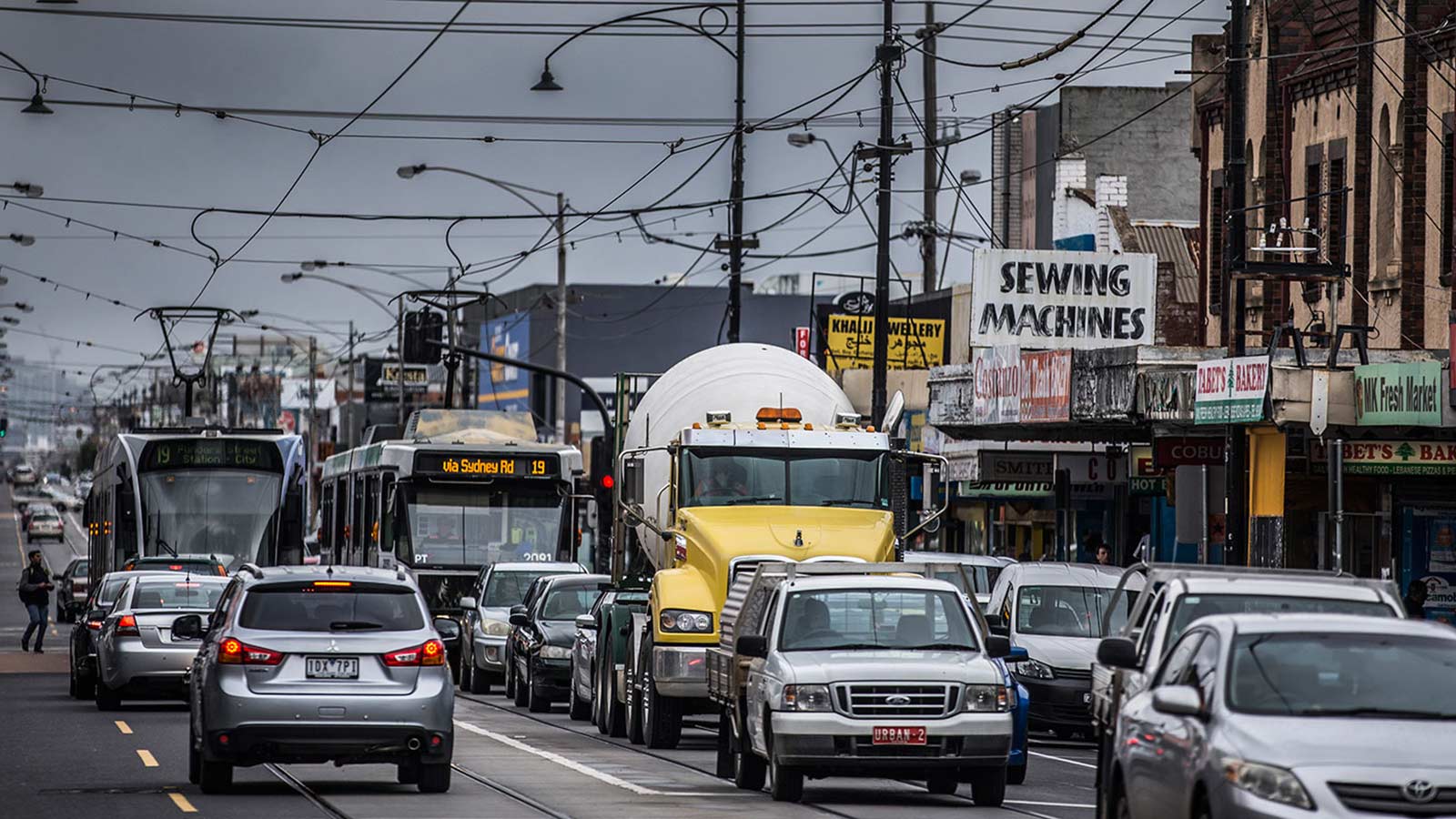Traffic congestion on a busy shopping street with cars, trams and a yellow cement truck.
