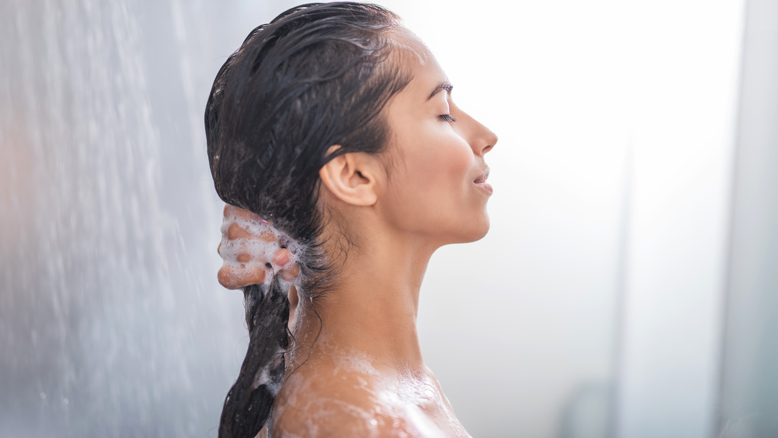 A person washing their hair with hot water from a shower.