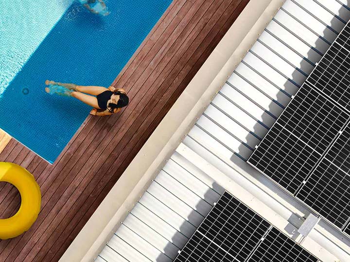 Aerial shot of a woman in pool alongside her house with solar panels