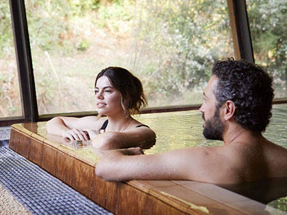 Couple sitting in the baths at Hepburn Springs, with nature surrounding them outside.