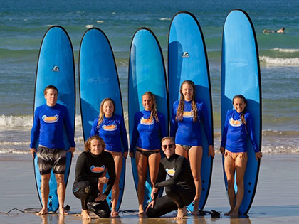 Group of surfers standing in front fo their surfboards in front of the water at the beach.