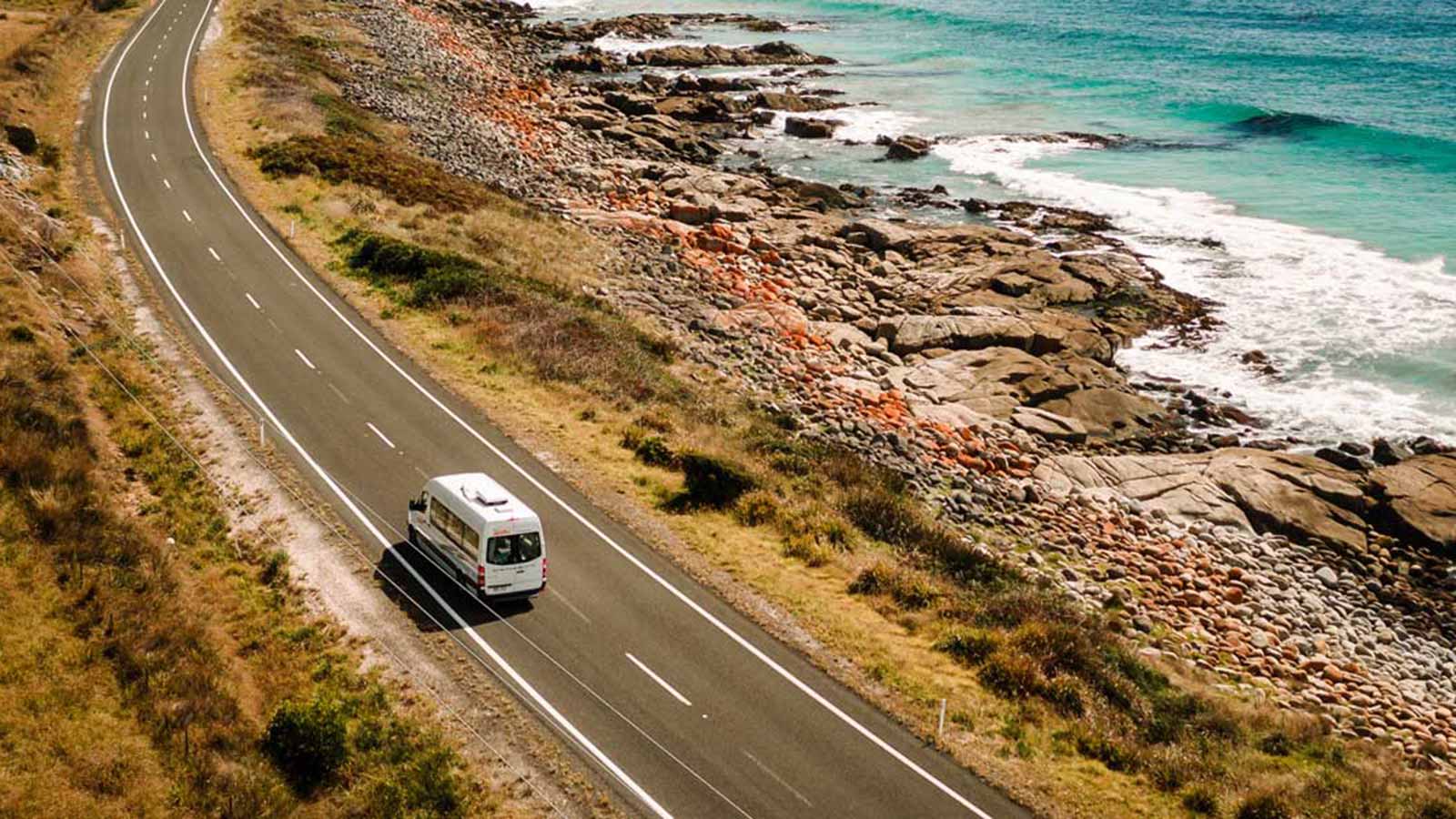 White campervan driving along ocean road.