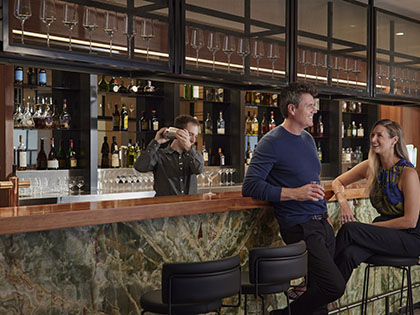 Couple sitting at bar at RACV Healesville's Banyalla Bar while bartneder shakes cocktail shaker.