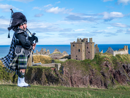 Traditional bagpiper in full dress code at Dunnottar Castle in Stonehaven