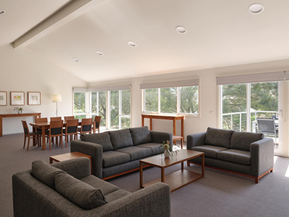 The living area of the 2-bedroom golf villa at RACV Cape Schanck Resort, featuring a dining table, couch and chairs with TV and stereo, and the balcony with outdoor dining.