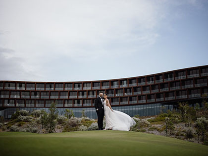 Couple posing on grass in front of RACV Cape Schanck resort, wearing wedding dress and suit.