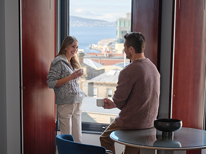 Couple standing by a window at RACV Hobart Hotel's King Room, holding mugs in their hands.