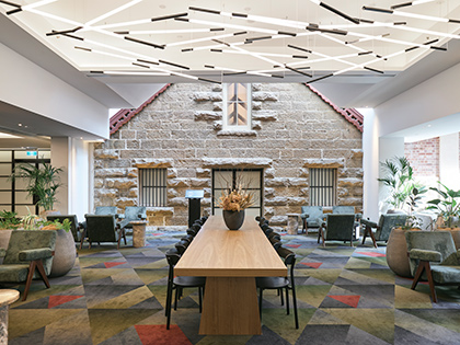 RACV Hobart Hotel lobby, featuring a long dining table with a floral centrepiece surrounded by couches, coffee tables and pot plants.