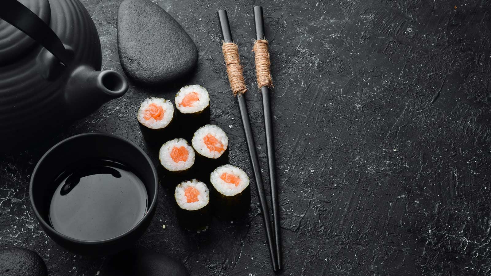 Sushi made with salmon next to chop sticks and a black teapot