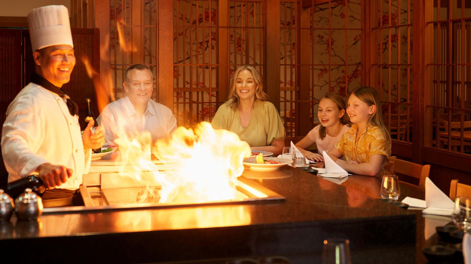 Family enjoying dinner at RACV Royal Pines Arakawa's teppanyaki table while watching chef flambé hot plate.
