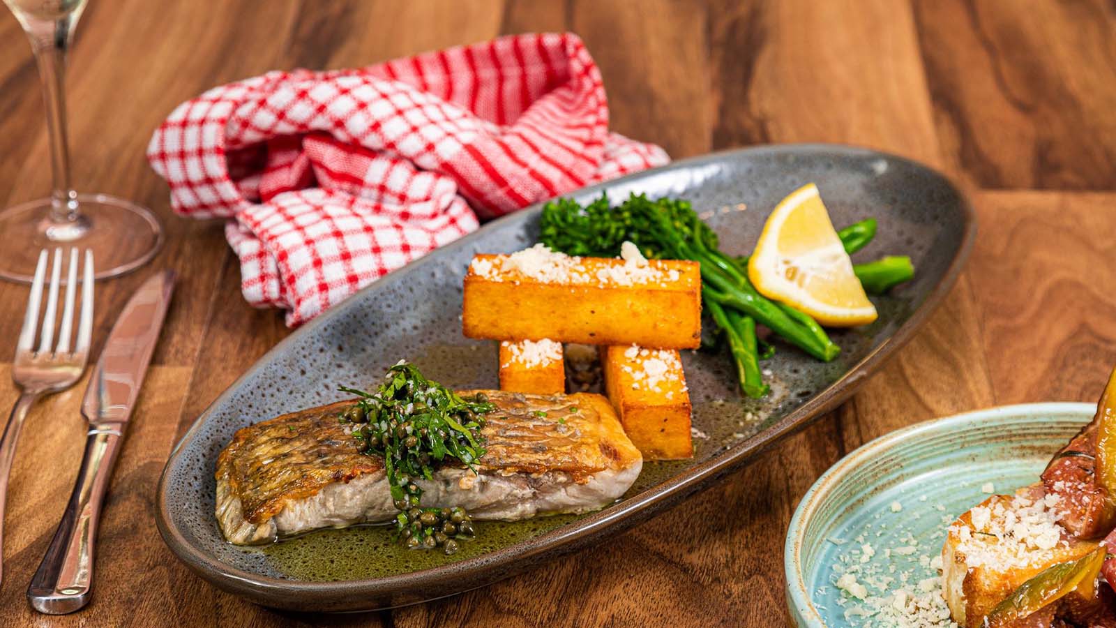Plated dish featuring fish and veggies, with a napkin and pair of cutlery beside.