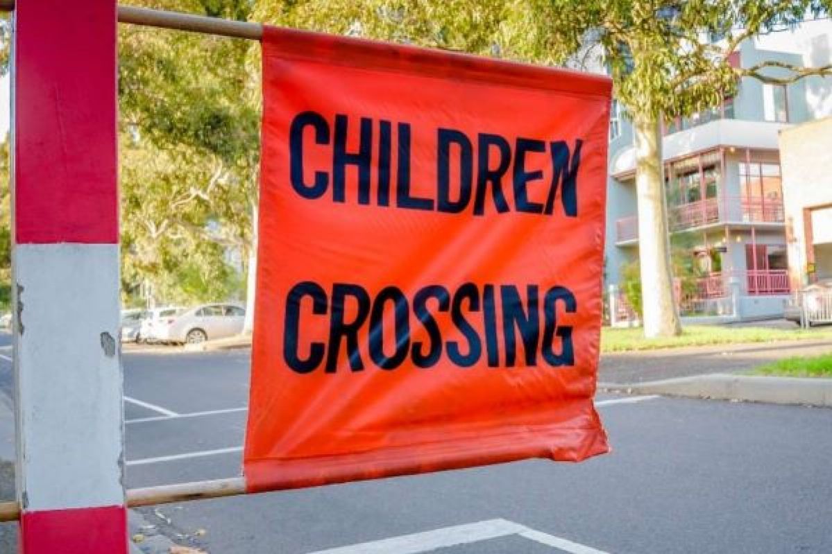 An orange flag with the words "children crossing" on it at a pedestrian crossing.