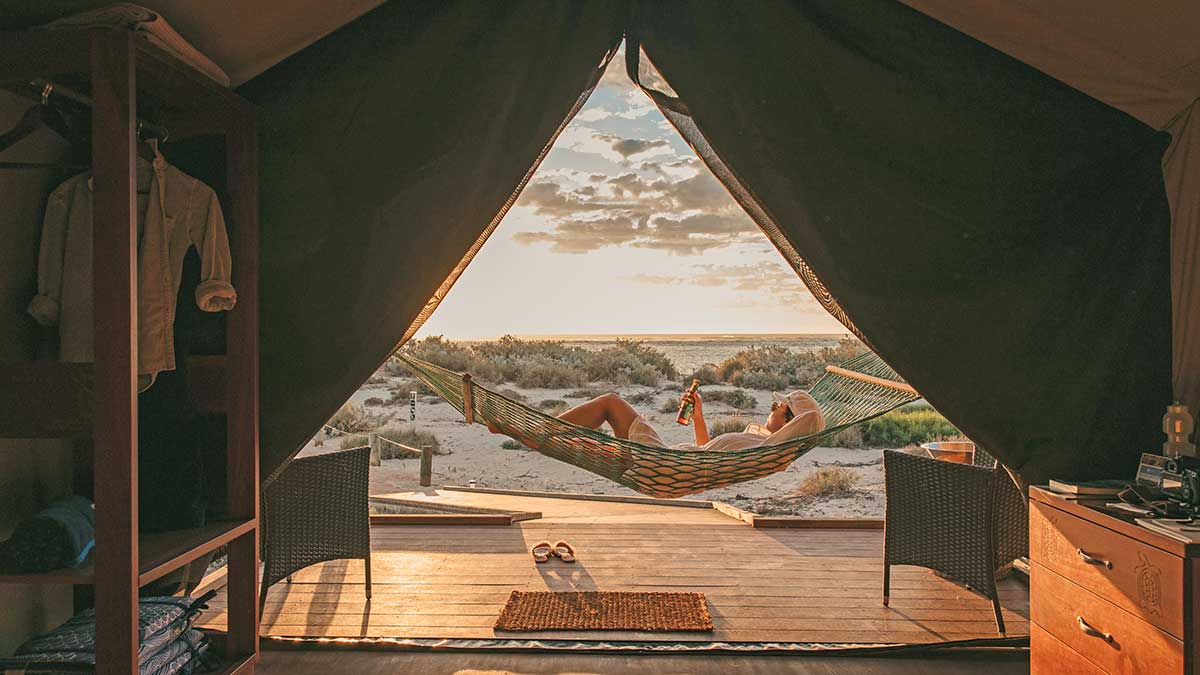 Woman on a hammock in front of a tent at sunset