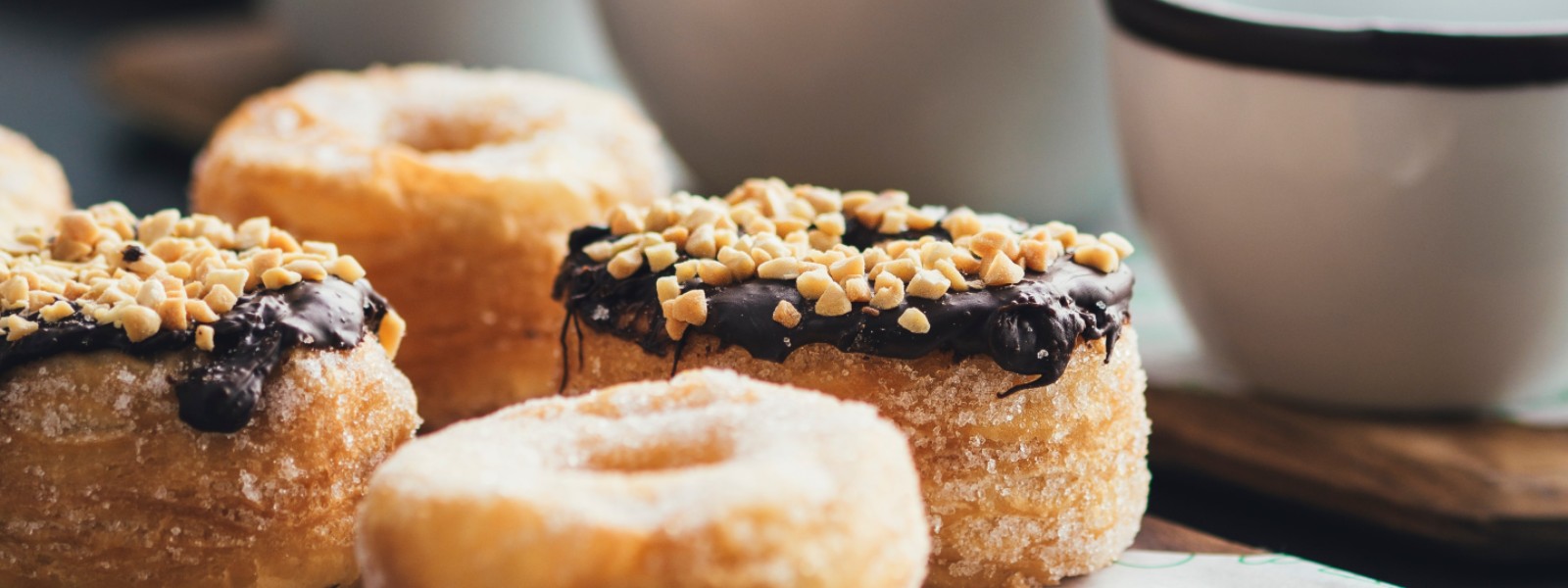 four sugared croissant doughnuts next to ceramic cups