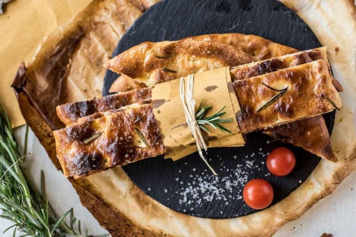 slats of rosemary focaccia bread tied up on a black plate next to rosemary sprigs