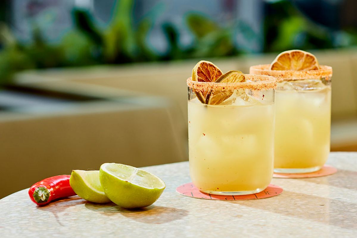 two spicy cocktails on a table with chilli and lime