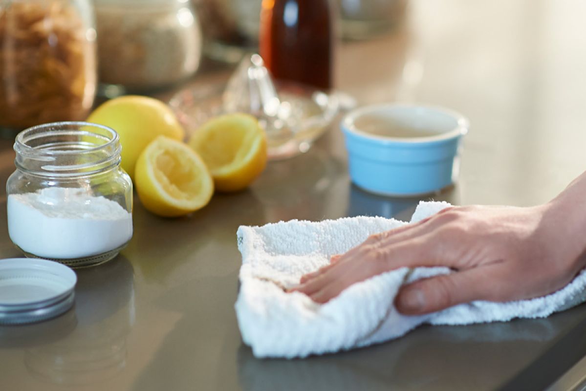 A person wiping down a bench that has a jar of bicarb soda and a cut lemon on it