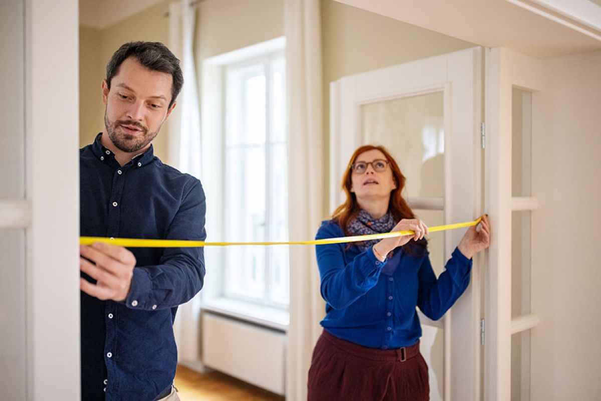 Man and woman measuring dimensions of a room with a measuring tape