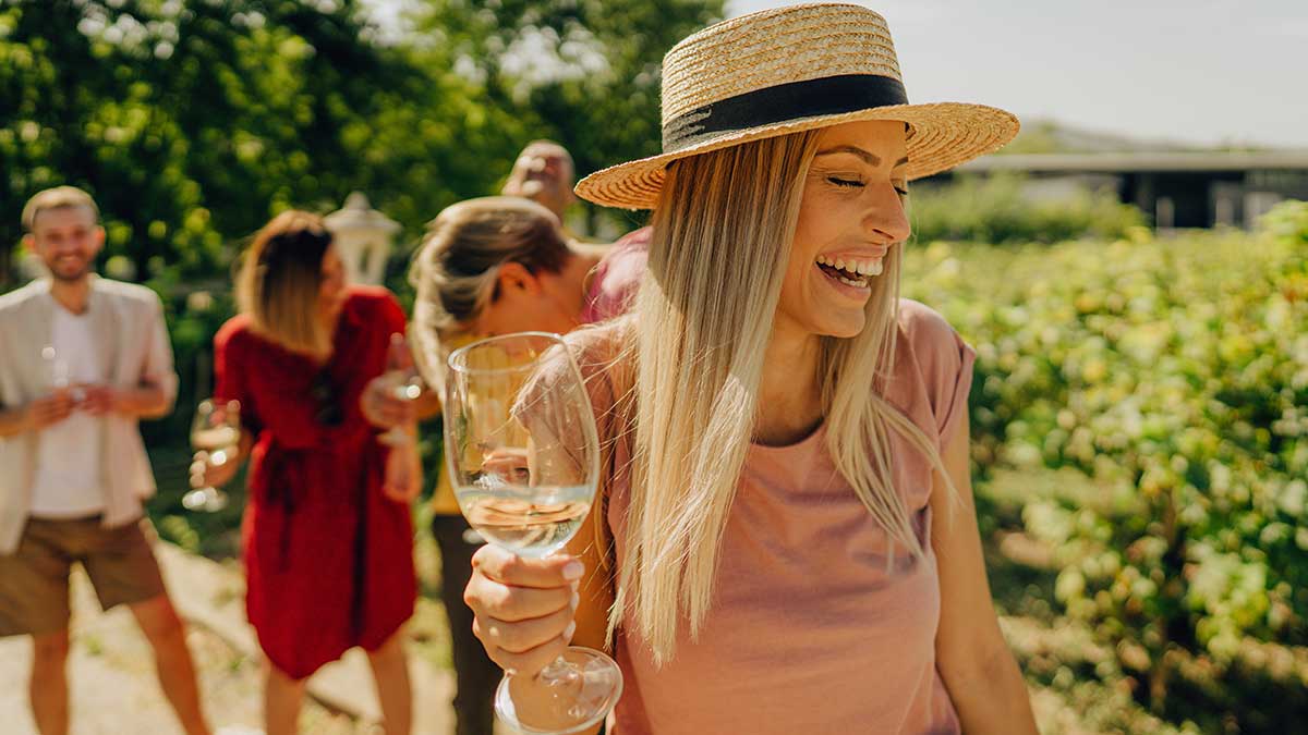 Woman laughing while holding a glass of white wine outdoors with three friends