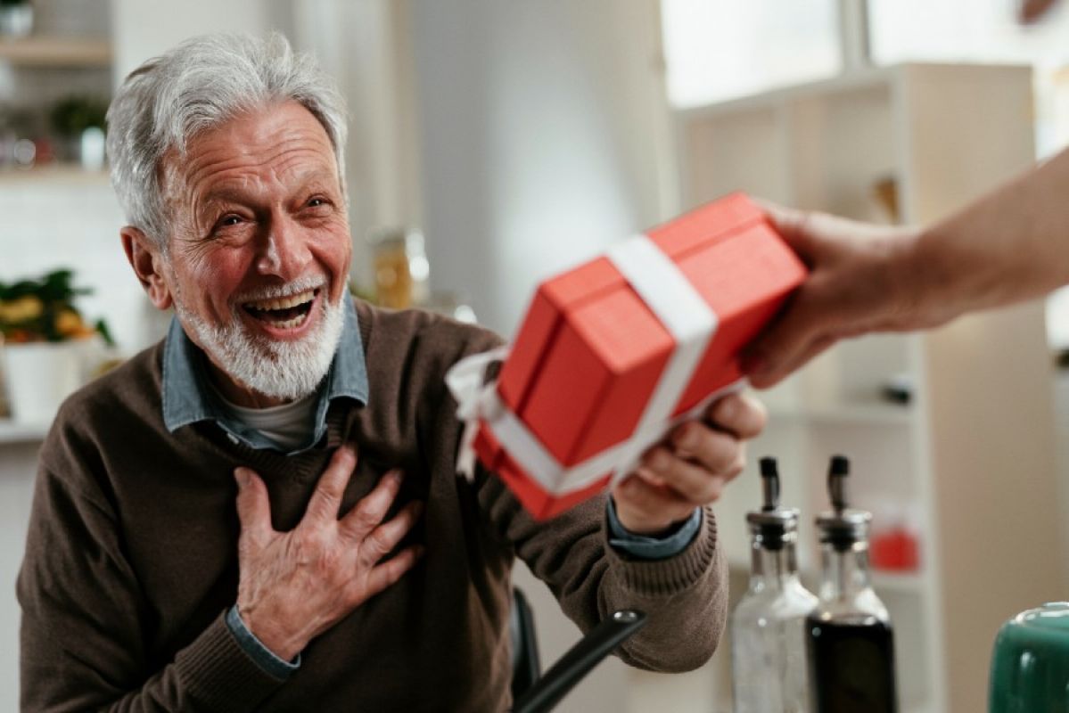 An elderly man smiling broadly as he receives a gift 