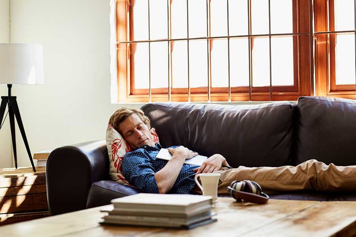 Man sleeping with book resting on his chest on the couch