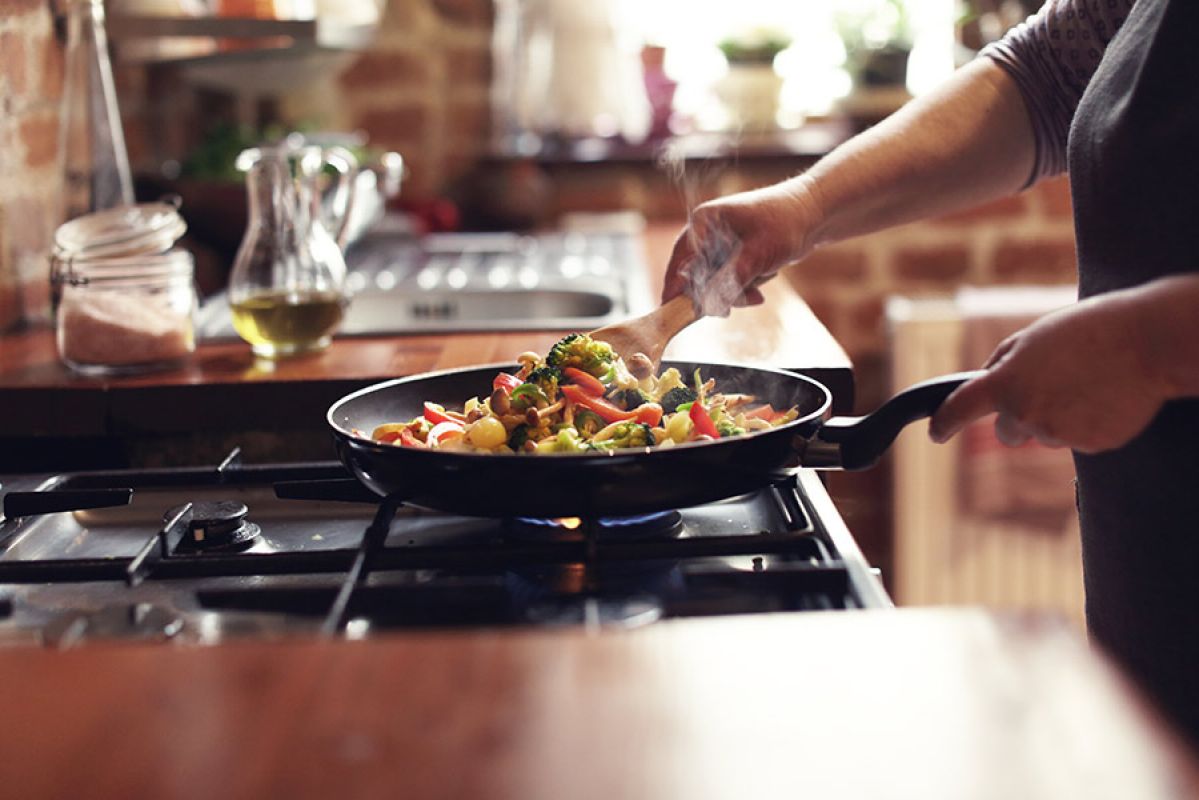 A person cooking a colourful vegetable stir fry in a pan on a gas stove