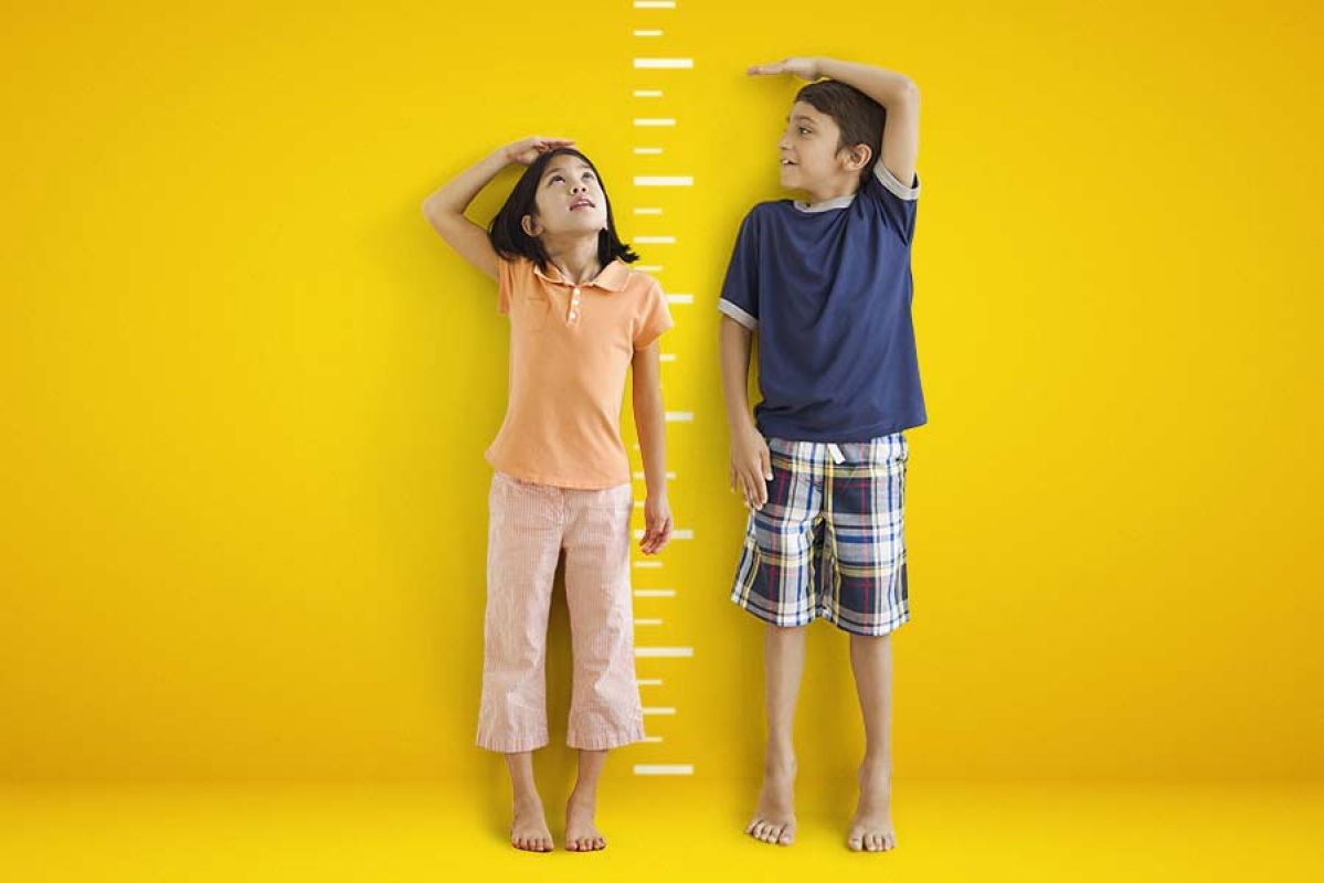 A boy and girl compare heights against a yellow background.