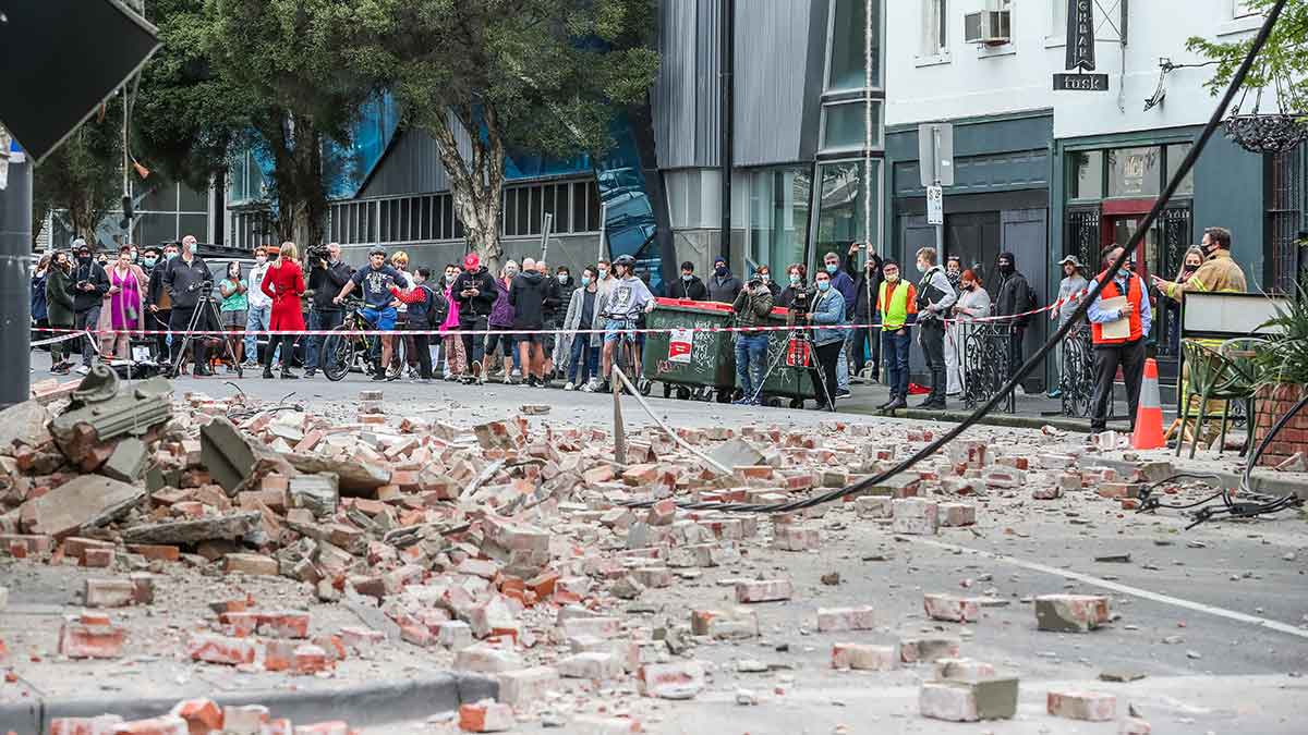 A crowd behind caution tape looking at debris from an earthquake