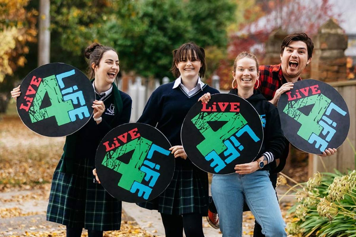 Four young people smiling while holding up circular 'Live4Life' signs