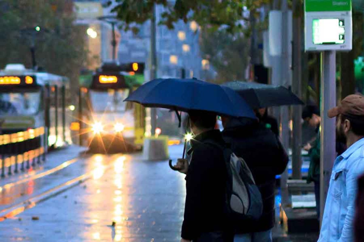 Man waiting for tram under umbrella in rain