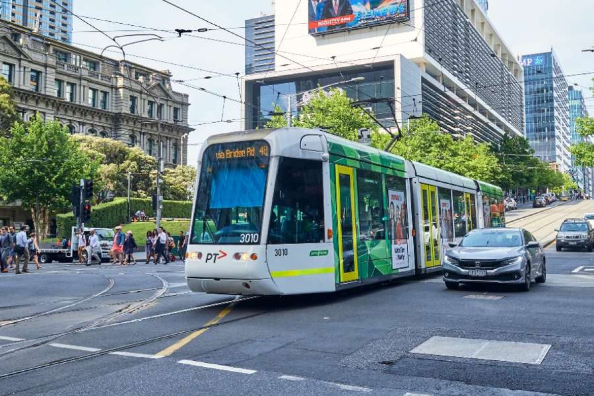 A tram travelling up Collins Street next to car traffic