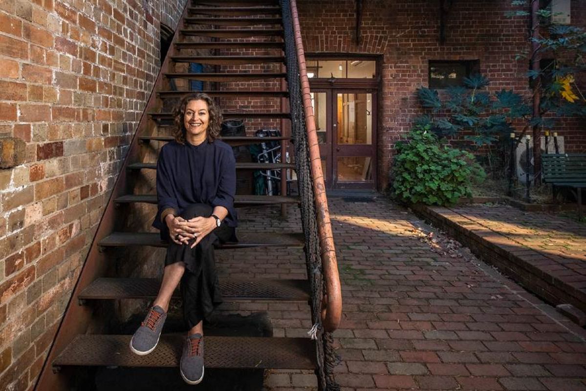 Woman sitting in backyard on wooden staircase next to red brick wall