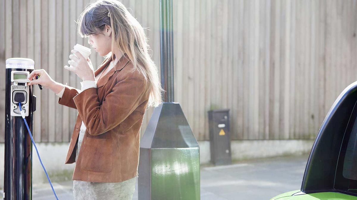 Woman drinking coffee while charging car