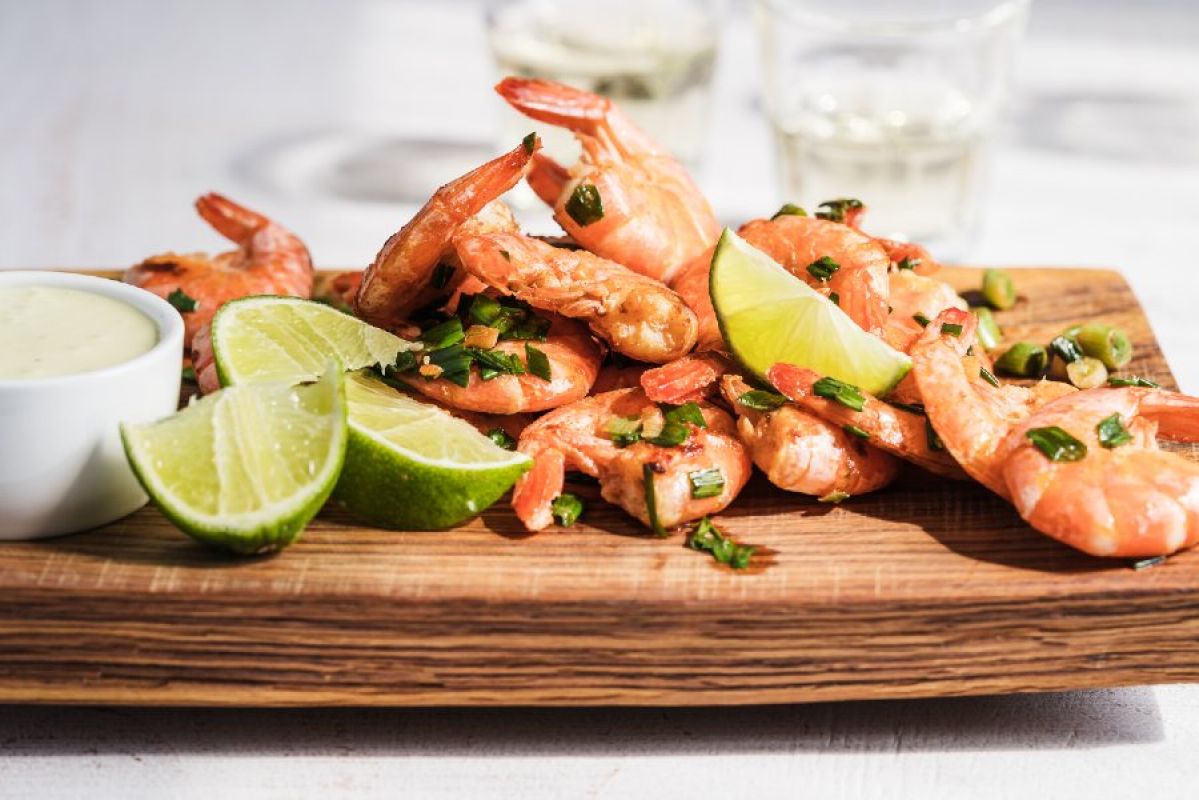 Cooked prawns on a wooden board with lime, herbs and mayo