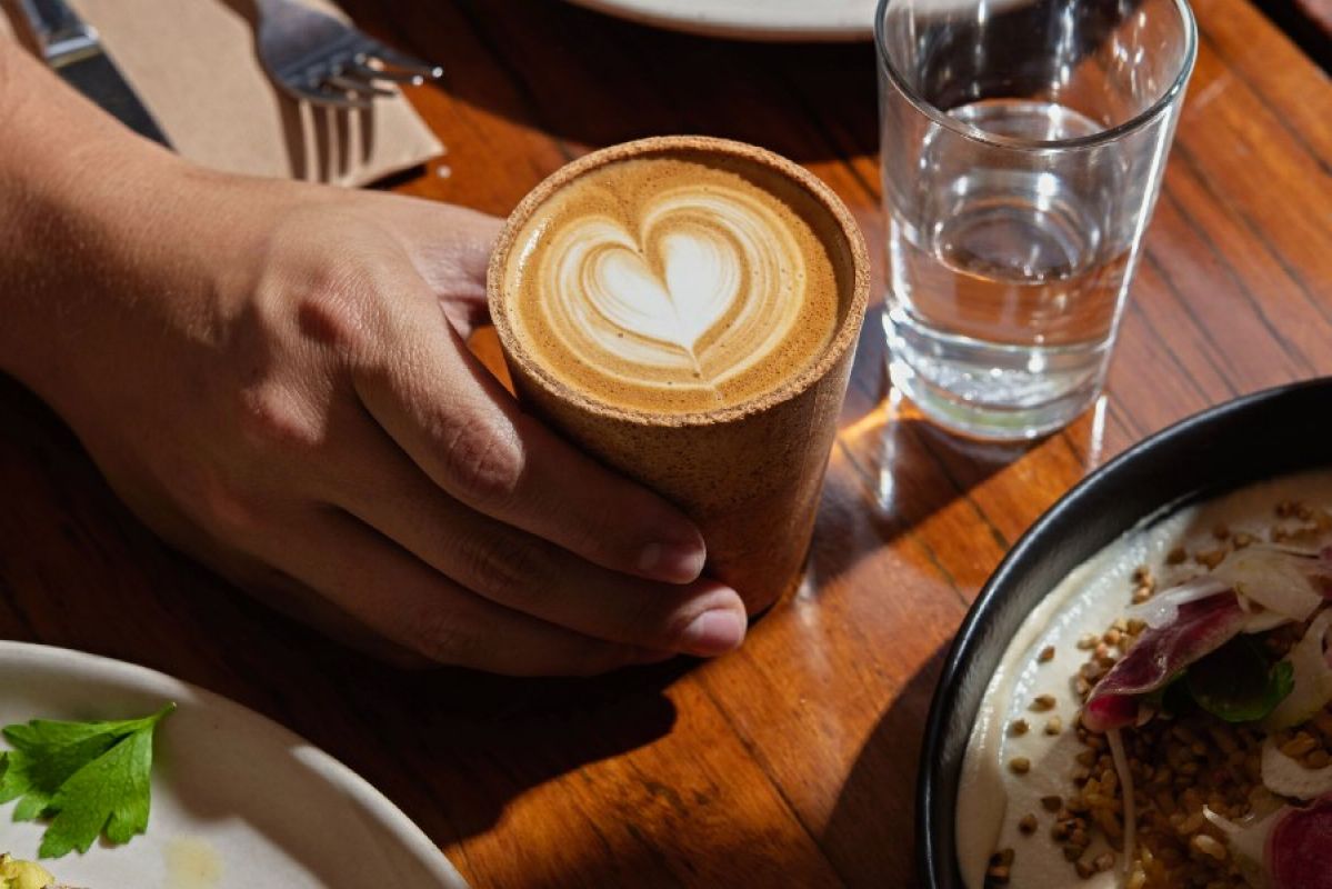 A hand places an edible coffee cup on a cafe table